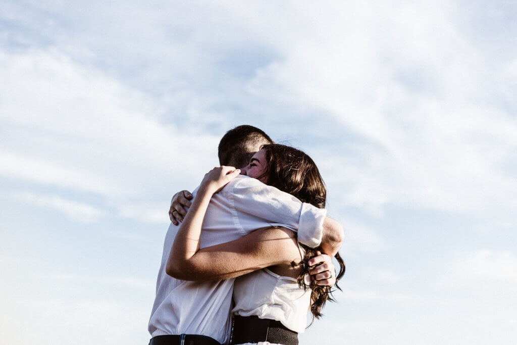 Man and woman hugging in front of blue skies